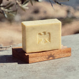 Bar of soap on a wooden stand with an eagle emblem, set against a natural background.