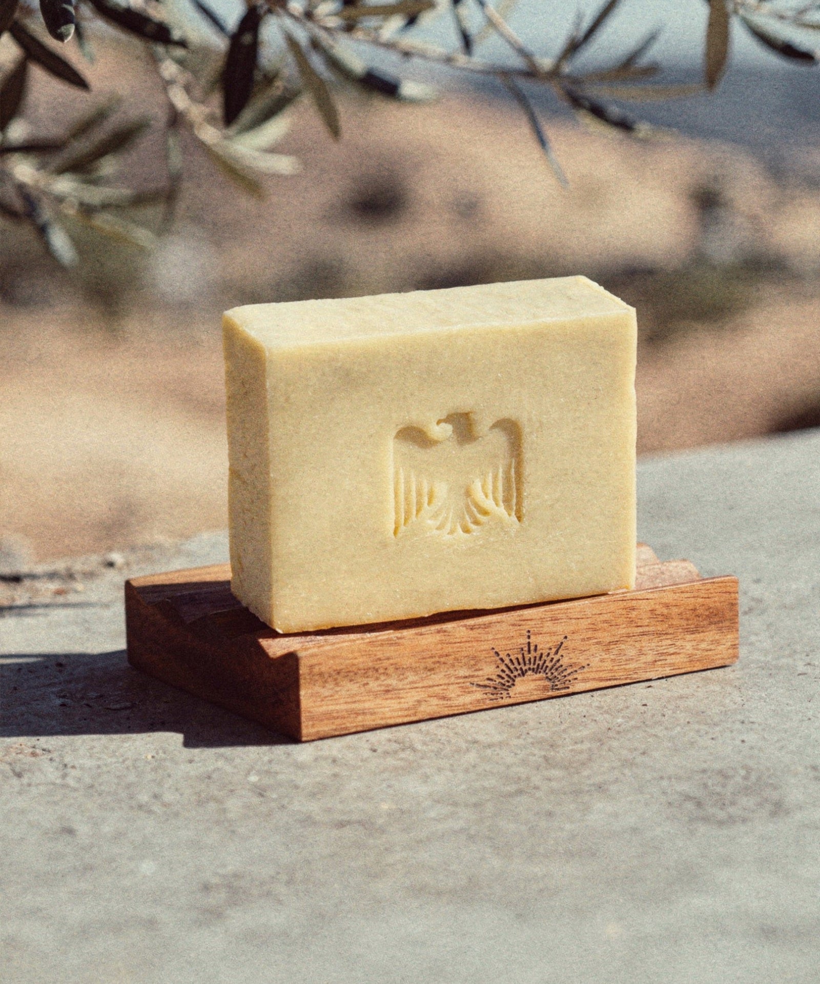 Bar of soap on a wooden stand with an eagle emblem, set against a natural background.