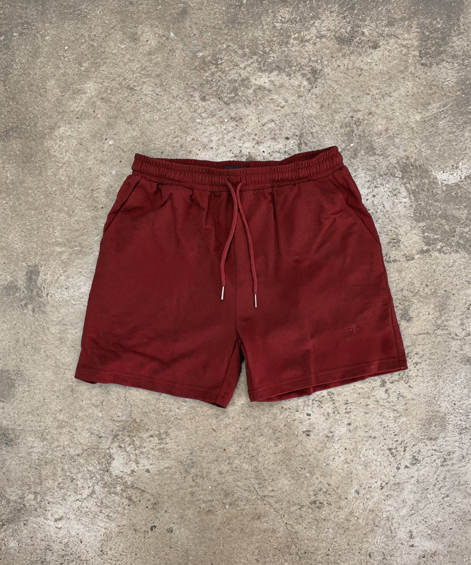 Blood red Sol Dept. cotton gym shorts on a gray concrete surface