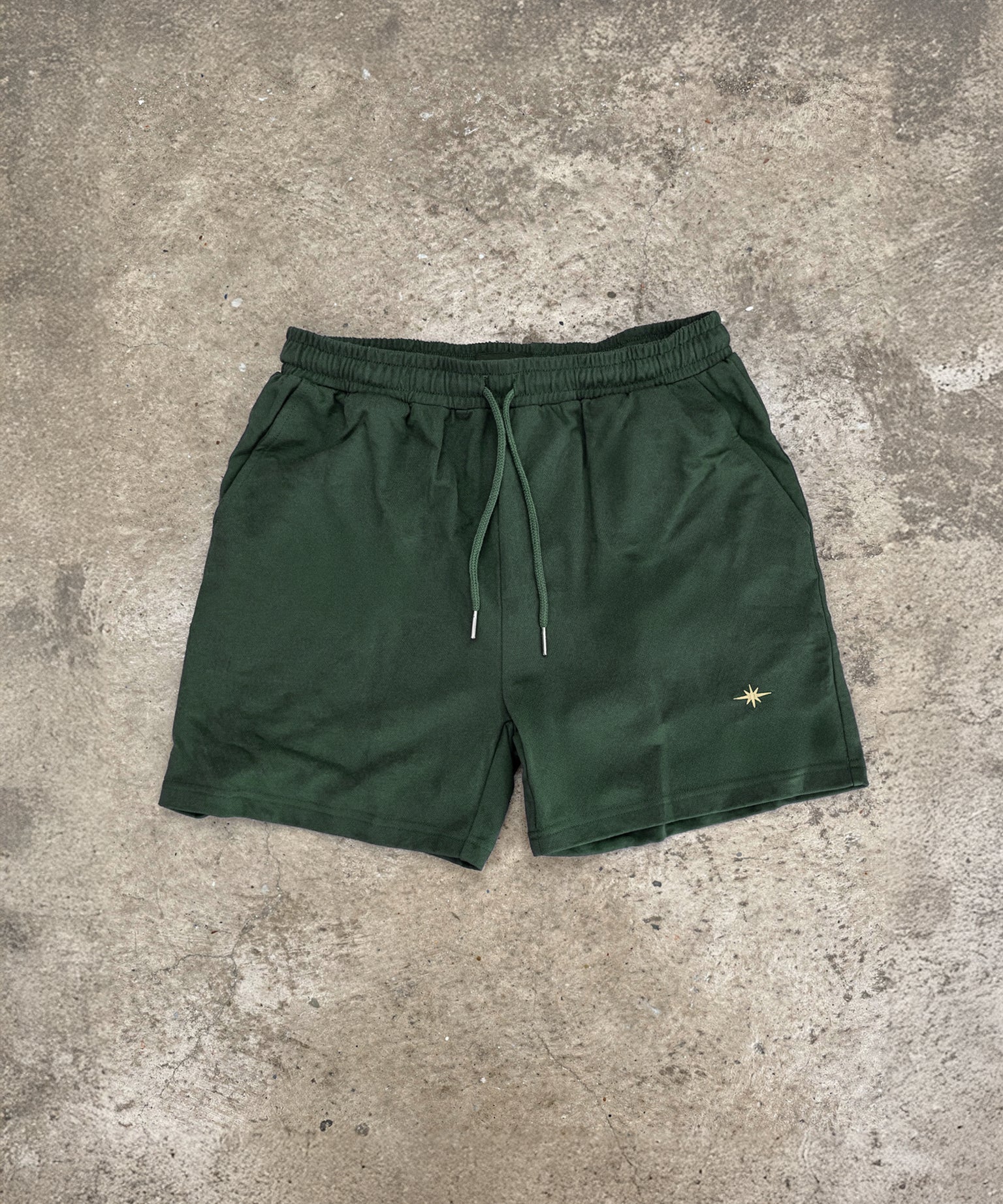 Forest green Sol Dept. cotton gym shorts on a gray concrete surface