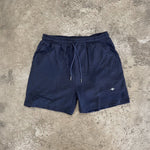 Navy blue shorts with a small white logo on a gray concrete surface