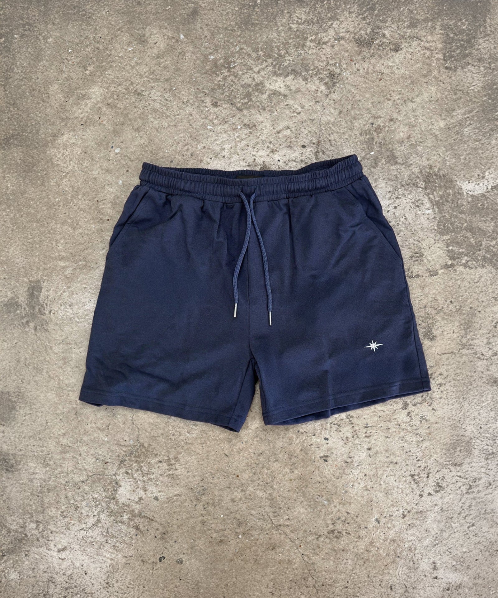 Navy blue shorts with a small white logo on a gray concrete surface