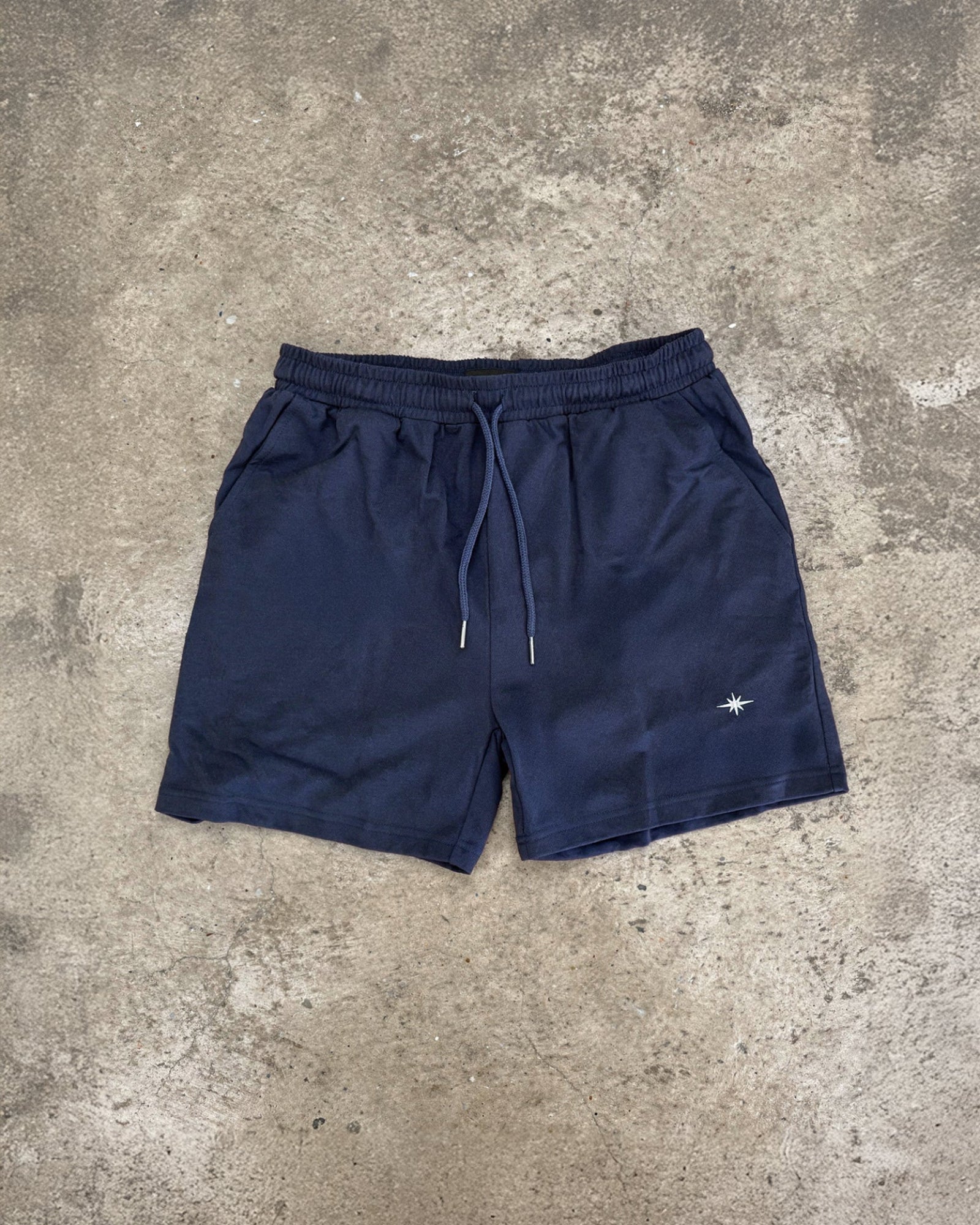 Navy blue shorts with a small white logo on a gray concrete surface