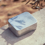 Metallic rectangular dish with embossed design on a concrete surface with blurred natural background