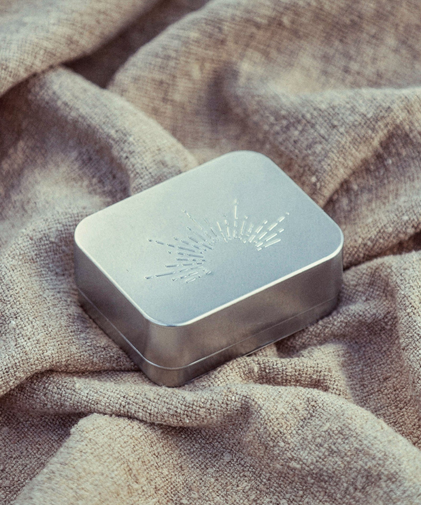Metallic rectangular box with engraved design on a textured fabric background