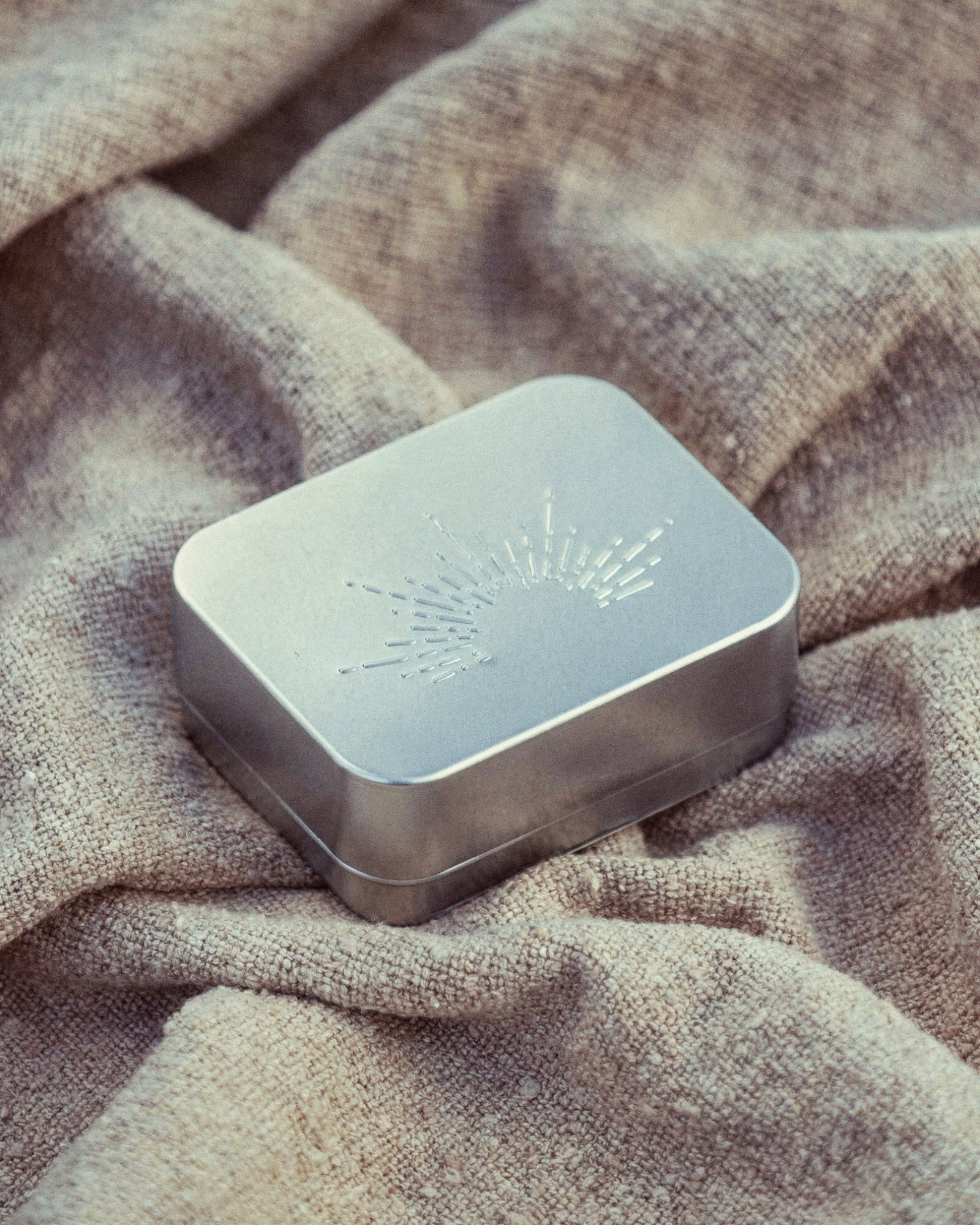 Metallic rectangular box with engraved design on a textured fabric background